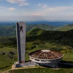 Висока телевизионна кула и обсерватория, разположени в планините на България, с гледка към зелени хълмове.