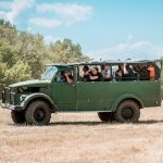 Зелена туристическа джип с група пътуващи хора на открито.