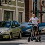 A chain on a city street with parked cars and a man driving an electric trolley.