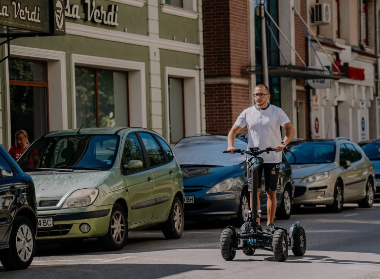 A chain on a city street with parked cars and a man driving an electric trolley.