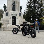 Електрически велосипед на фон в градска среда, туристи и историческа забележителност.