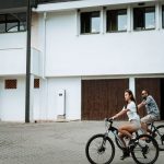 Мъже и жена каращи велосипеди пред съвременна сграда, екологичен транспорт.