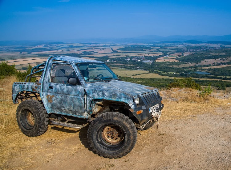 стар бял джип с големи off-road гуми в планински пейзаж България.