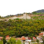 старинна крепост на хълм, околните къщи, зеленина, село в България.